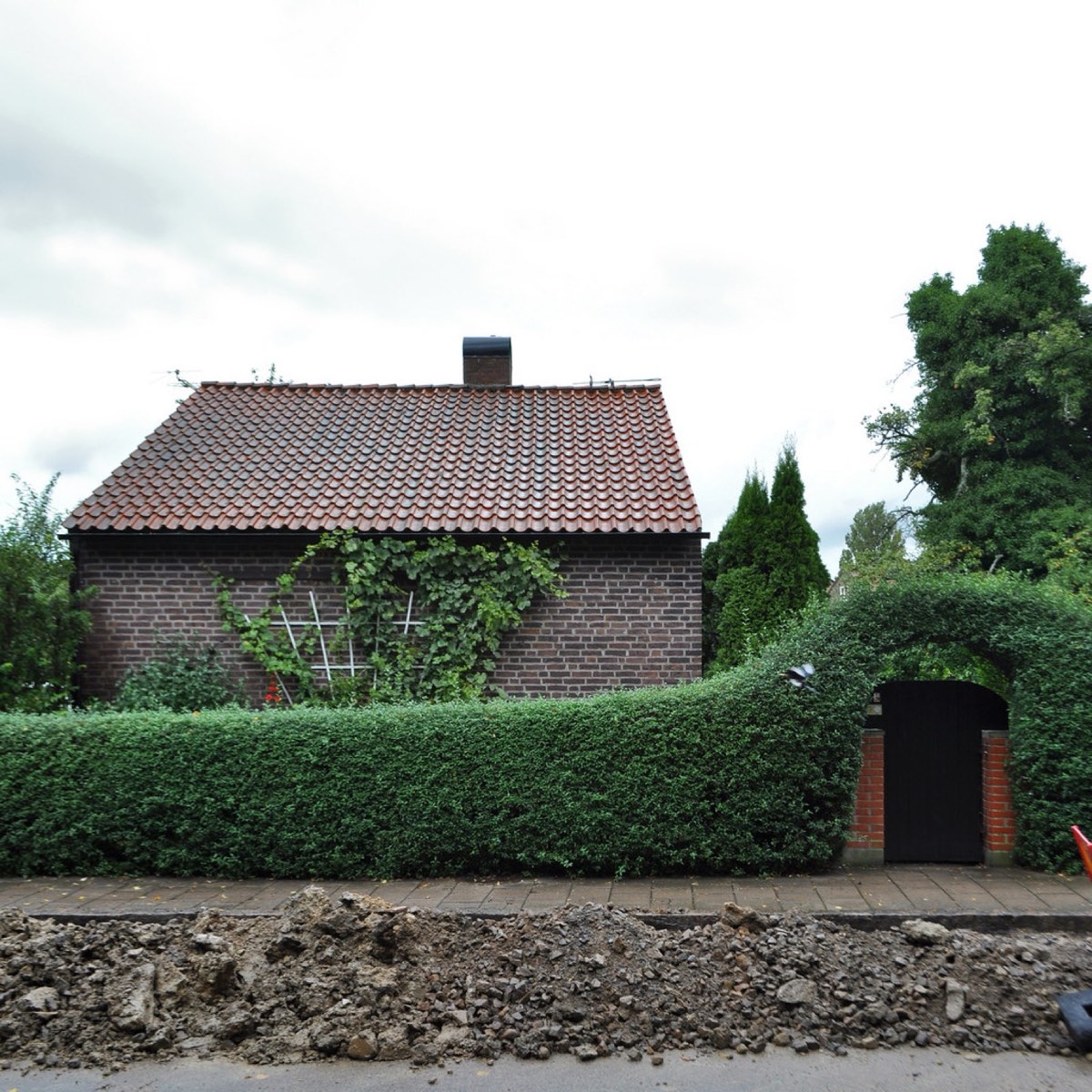 Einfamilienhaus aus Backstein mit grüner Hecke an einer Wohnstraße